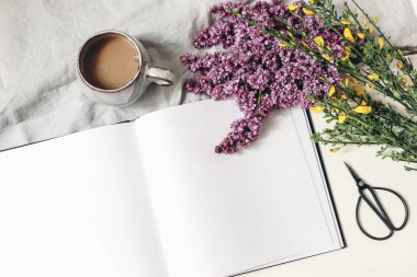 Stili bahar kahvaltısı sahnesi, kadınsı çiçek kompozisyonu. Mor leylak dalları buketi, sarı süpürge Cytisus, bir fincan kahve, beyaz masa arkasında izole edilmiş keten masa örtüsü. Düz yatıyordu, üst.