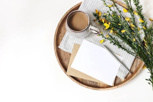 Petit déjeuner de printemps. Balai jaune branches Cytisus, serviette en lin, tasse de café, plateau en bois isolé sur fond de table blanc. Carte de vœux vierge et maquette de l'enveloppe. Appartement de Pâques, vue sur le dessus . — Photo