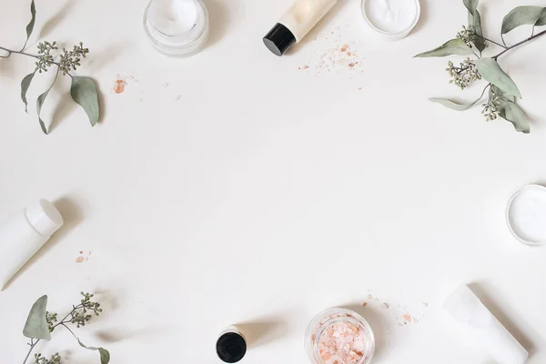 Hudkräm, schampo flaska, torra eukalyptus blad och rosa Himalaya salt. Vit tabell bakgrund. Stylad skönhetsram, web banner. Ekologisk kosmetika, spa-koncept. Tomrum, platt ligg, ovanifrån. — Stockfoto