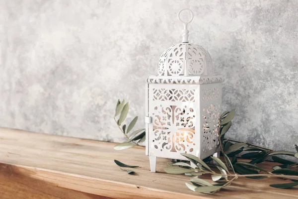 White ornamental Moroccan, Arabic lantern. Green olive leaves, branches on old wooden table, blurred grunge wall background,. Greeting card for Muslim holiday Ramadan Kareem. Festive still life. — Stock Photo, Image