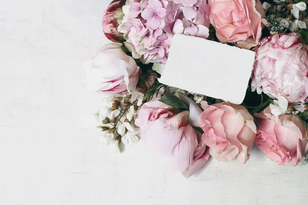 Casamento, aniversário de papelaria cena mock-up. Cartão de saudação em branco, convite. Canto floral decorativo de rosas rosa, peônias, hortênsias e flores de gafanhotos no fundo de madeira velho. Vista superior . — Fotografia de Stock