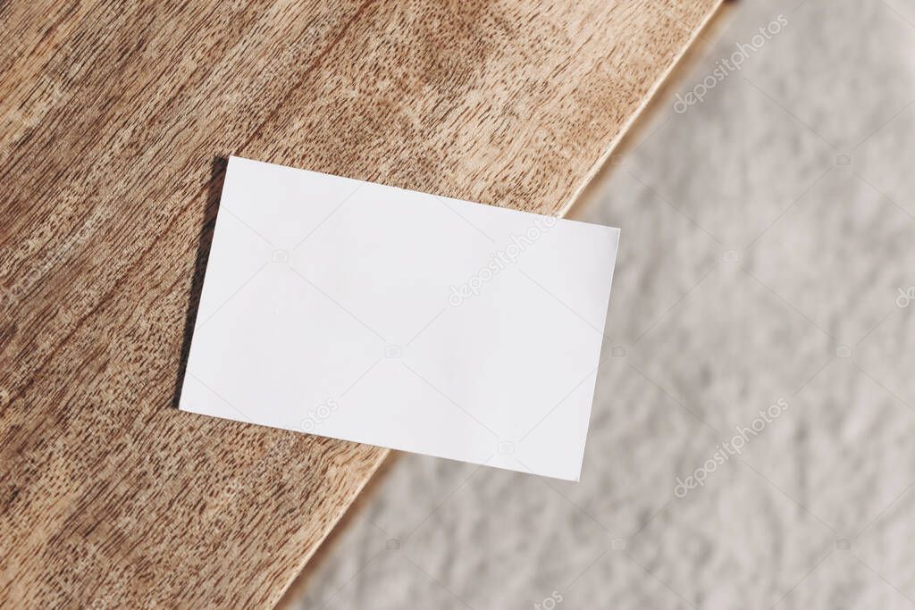 Closeup of blank business card on teak wooden table. Blurred beige linen background. Empty paper card mockup scene in neutral colors. Branding, business concept. Sparse composition Top view.