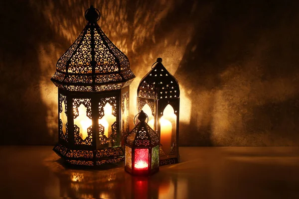 Ornamental Arabic lanterns with burning candles on table glowing at night. Festive greeting card, invitation for Muslim holy month Ramadan Kareem. Iftar dinner background with golden glow. — Stock Photo, Image