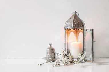 Gümüş süslemeli çay, beyaz çiçekler, erik ağacı çiçekleri ve masa arkasında parlayan Fas feneri. Havan topu yemeği. Ramazan Kareem tebrik kartı, davetiye. Fitr müslüman bayramı.