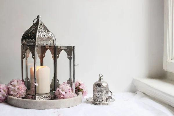 Taza decorativa de plata de té, flores de cerezo rosa y linterna marroquí brillante en manteles de lino cerca de la ventana. Iftar cena. Tarjeta de felicitación Ramadán Kareem, invitación. Vacaciones Eid ul Fitr . — Foto de Stock