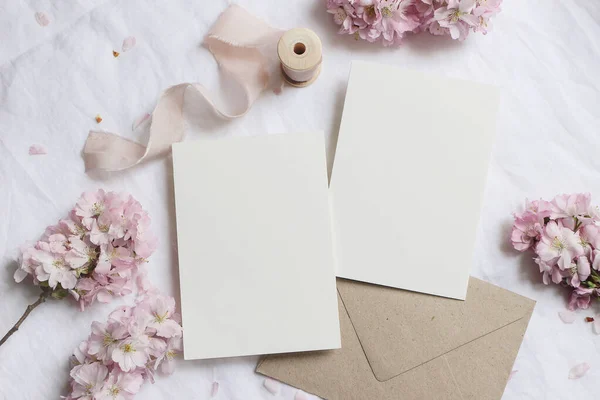Bröllop brevpapper prototyp scen. Blank gratulationskort, kuvert på linneduk bakgrund med rosa blommande körsbärsträd grenar och band. Feminin stilleben sammansättning. Platt ligg, ovanifrån — Stockfoto
