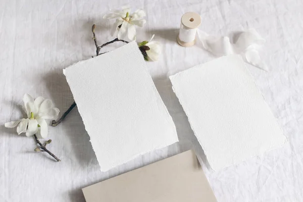 Papelaria de casamento. Cena recheada com cartões de papel em branco, envelope no fundo da toalha de linho. Magnolia stellata branco galhos de árvores e fita. Feminino ainda vida, flat lay, topo . — Fotografia de Stock