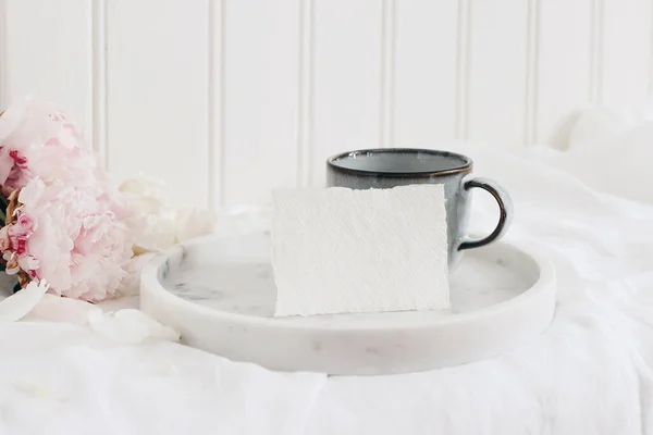 Scena di natura morta di matrimonio. Business, place card mockup scene, vassoio di marmo, tazza di caffè e fiori di peonia rosa su tovaglia di lino bianco. Vintage foto in stile femminile. Composizione festiva floreale . — Foto Stock