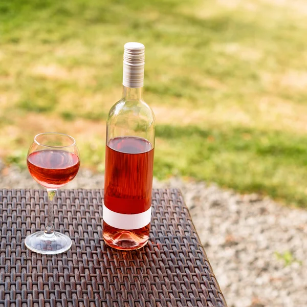 Una copa y una botella de vino tinto o rosa en el viñedo de otoño en la mesa de mimbre de madera. Tiempo de cosecha, picnic, tema del festival . — Foto de Stock