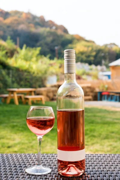 Um copo e garrafa de vinho tinto ou rosa em vinhedo de outono na mesa de vime de madeira. Tempo de colheita, piquenique, tema de festa . — Fotografia de Stock