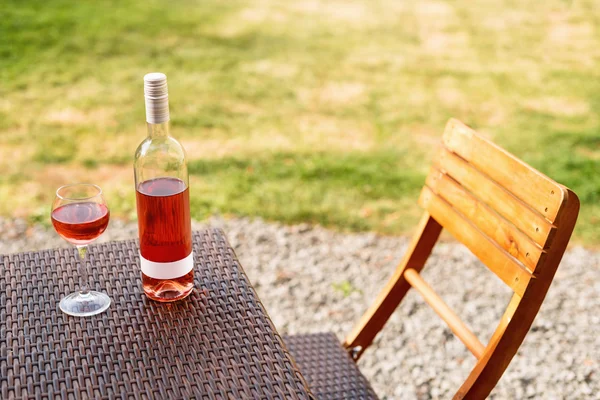 One glass and bottle of red or rose wine in autumn vineyard on wooden wicker table. Harvest time, picnic, fest theme. — Stock Photo, Image