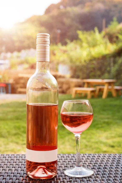 Um copo e garrafa de vinho tinto ou rosa em vinhedo de outono na mesa de vime de madeira. Tempo de colheita, piquenique, tema de festa . — Fotografia de Stock