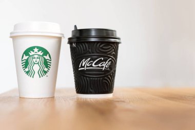 Kiev, Ukrayna: 06 Kasım 2019: Bir fincan Starbucks kahvesi ve McDonald 's kahvesi açık arkaplanda, ahşap masa üzerinde. Marka çatışması, müşteri seçimi ve küreselleşme kavramı.