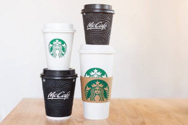 Kiev, Ukrayna: 06 Kasım 2019: Dört fincan Starbucks kahvesi ve McDonald 's kahvesi açık arkaplanlı ahşap masa üzerinde. Marka çatışması, müşteri seçimi ve küreselleşme kavramı.