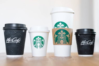 Kiev, Ukrayna: 06 Kasım 2019: Dört fincan Starbucks kahvesi ve McDonald 's kahvesi açık arkaplanlı ahşap masa üzerinde. Marka çatışması, müşteri seçimi ve küreselleşme kavramı.