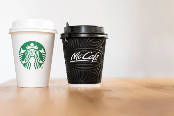 KIEV, UCRANIA: 06 de noviembre de 2019: Una taza de café Starbucks y café McDonald 's sobre mesa de madera sobre fondo claro. Confrontación de marca, elección del cliente y concepto de globalización . —  Fotos de Stock