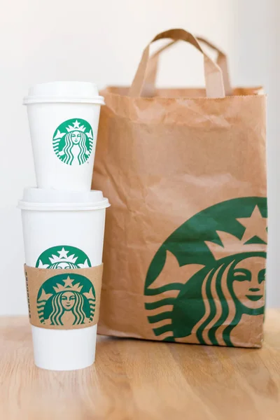 KIEV, UCRANIA: 06 de noviembre de 2019: Starbucks Café para llevar tazas con bolsa de papel sobre mesita de madera. American global coffee and coffeehouse company, fundada en Seattle, Wa. Estados Unidos, en 1971 — Foto de Stock