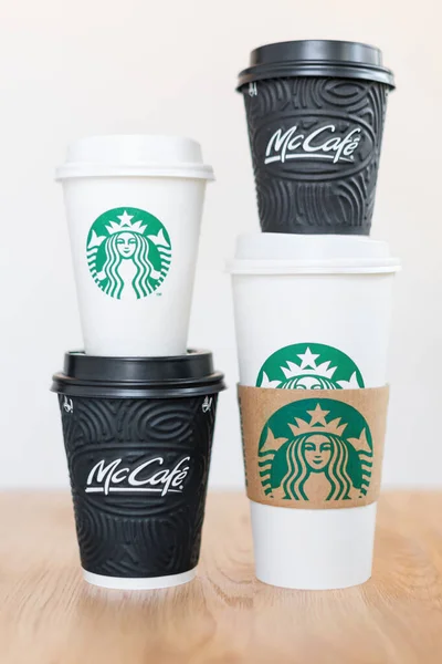KIEV, UCRANIA: 06 de noviembre de 2019: Cuatro tazas de café Starbucks y café McDonald 's sobre mesa de madera sobre fondo claro. Confrontación de marca, elección del cliente y concepto de globalización . — Foto de Stock