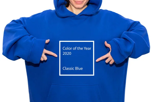 Menina jovem hipster vestindo capuz azul e apontando os dedos no texto Cor do Ano 2020 clássico azul. Mulher apontando para o peito com as duas mãos, próximo trand na cor . — Fotografia de Stock