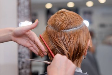 Yeni saç kesimi yaptıran bir kadın. Kuaförde saç kesen kadın kuaför. Kuaför, el ele tutuşup saç, tarak ve makas arasına girer..