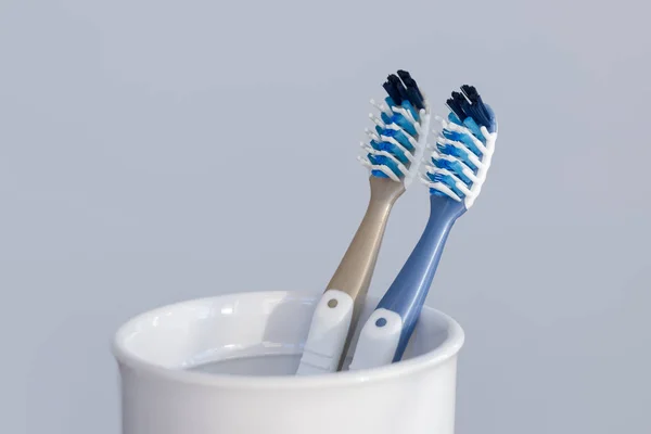 Two plastic toothbrushes in toothbrush cup closeup on grey background — Stock Photo, Image