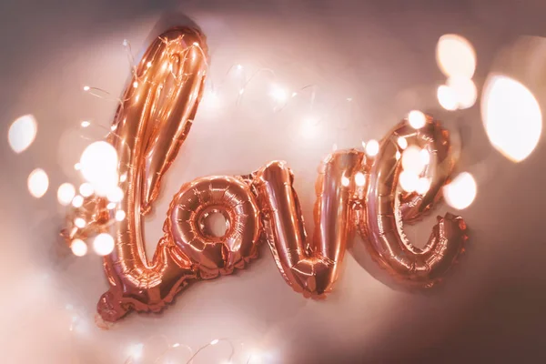 Rose gold foil balloon in the form of a word Love with light garland. Happy Valentine day. Word love letters from the inflatable balloons with bokeh — Stock Photo, Image