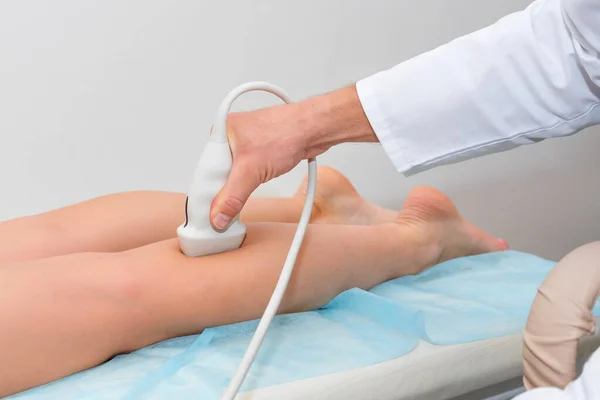 Lekarz w białym mundurze ze sprzętem diagnostycznym wykonuje USG za pomocą urządzenia na nogach pacjentki. Chirurg, flebolog pracujący w klinice. Narzędzia medyczne w szpitalu. — Zdjęcie stockowe