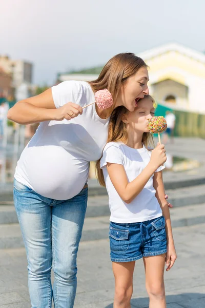 かわいい女の子と妊娠中の母親は遊園地でキャンディリンゴを食べています 家族を愛してる お母さんと娘が一緒に楽しんでる — ストック写真