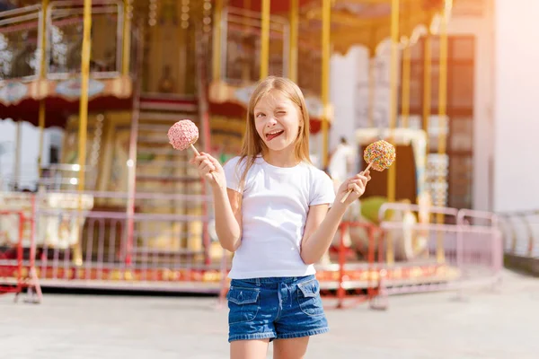 かわいい女の子食べるキャンディーアップルとポージングでフェアで遊園地 — ストック写真