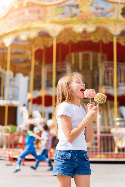 かわいい女の子食べるキャンディーアップルとポージングでフェアで遊園地 — ストック写真