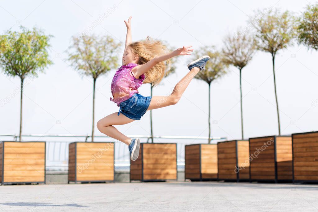 Active kid girl gymnast jumping or dancing on the street. Young girl acrobat. The girl is engaged in gymnastics
