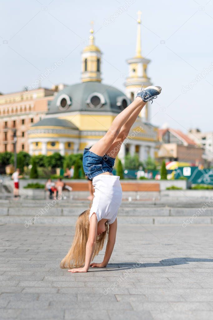 Active kid girl gymnast stretching and doing splits on the street. Young girl acrobat. The girl is engaged in gymnastics