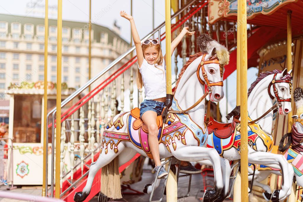 Girl riding on a merry go round. Little girl playing on carousel, summer fun, happy childhood and vacation concept.