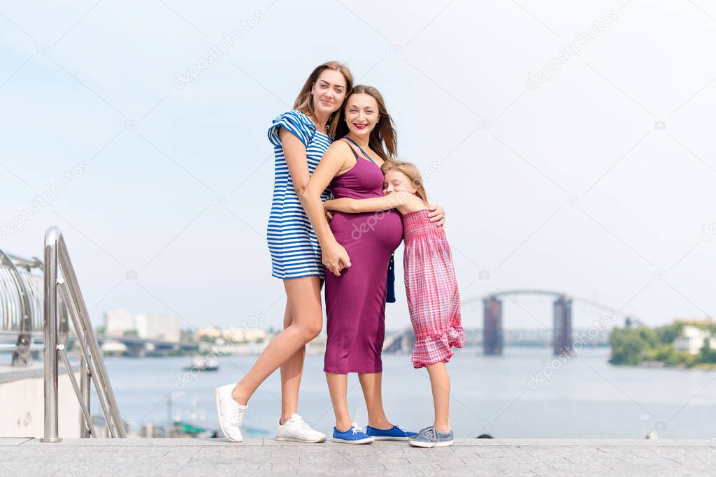 Samesex lesbian family with child on a walk in the park near the river. Lesbians mothers with adopted child, happy family, pregnant couple with kid