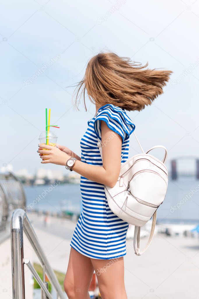 Pretty young woman drinking fruit cocktail and enjoying sun and good warm day near the river, summer vacation, woman relaxing outdoors