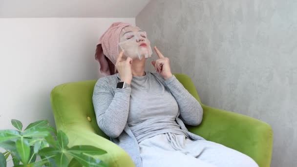 Jovem mulher aplicando cosméticos japonês ou coreana máscara em seu rosto em casa e descansando. Mulher rotina de beleza, descanso em casa. Auto isolamento, quarentena doméstica, distanciamento social — Vídeo de Stock