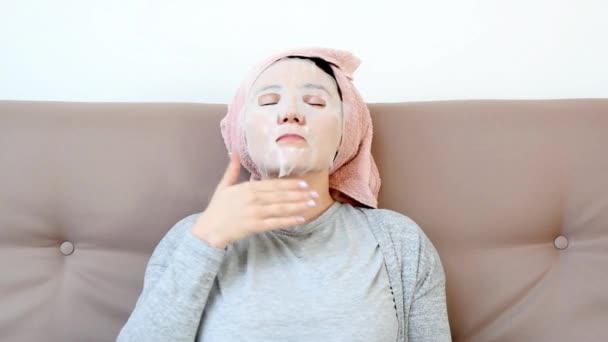 Mujer joven aplicando japanese cosmético o máscara de coreano en su cara en casa y descansando en el sofá. Rutinaria de belleza femenina, descanso en casa. Autoaislamiento, cuarentena doméstica, distanciamiento social — Vídeos de Stock