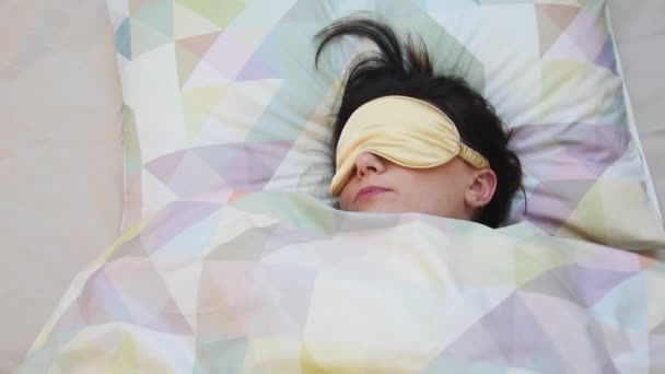 Κάτοψη της νεαρής γυναίκας που ξυπνάει το πρωί, φοράει μάσκα ύπνου και τεντώνεται μετά τον ύπνο. Ύπνος γυναίκα σε μάσκα ύπνου, τον τρόπο ζωής και τους ανθρώπους έννοια — Αρχείο Βίντεο