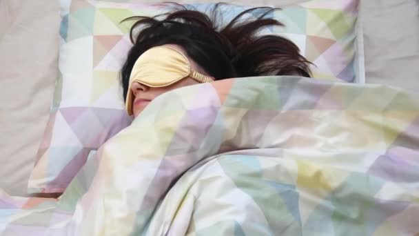 Вид сверху на молодую женщину, просыпающуюся утром, снимающую маску для сна и растягивающуюся после сна. Спящая женщина в маске, образ жизни и понятие людей — стоковое видео