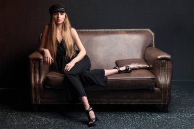 Sarışın model, karanlık stüdyoda koltukta poz veriyor. Karanlık arka planda poz veren genç çekici manken. Metin için boşluk.