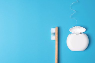 Diş ipi kabı ve mavi arka planda bambu diş fırçası. Günlük ağız temizliği, diş bakımı ve sağlık. Ağız temizleme ürünleri. Diş bakımı konsepti. Metin veya logo için boş yer.
