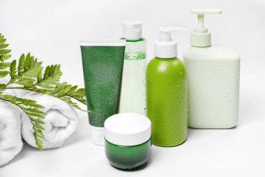 Yeşil bitkisel yaprakları ve beyaz havluları olan kozmetik kapları, markalaşma için boş etiket paketi. Nemlendirici krem, şampuan, tonik, yüz ve vücut bakımı. Doğal organik güzellik ürünleri