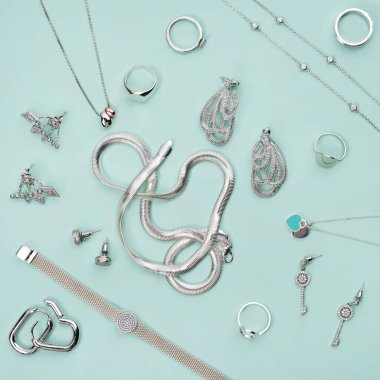 Minimum mavi arka planda gümüş mücevherler. Yüzükler, bilezikler ve küpeler. Moda kadını aksesuarlarının, mücevherlerin ve alışveriş konseptinin en üst görüntüsü. Moda minimalist geometrik düz konum