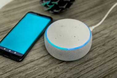 Amazon yankı noktası, ses kontrollü hoparlör aktif ses tanıma özelliği olan, ahşap arka planda mavi telefonun yanında