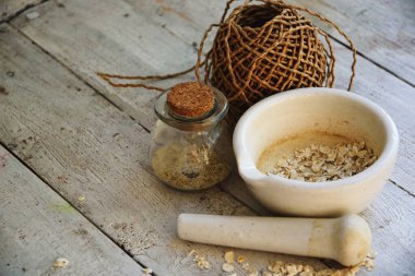 Doğal kozmetik yıkama konsepti için yulaf ezmesi tozu. İçine yulaf ezmesi dökülen beyaz bir havan topu, içine ubtan döküldüğü mantarlı yuvarlak bir cam şişe, bir rulo kağıt ambalaj.