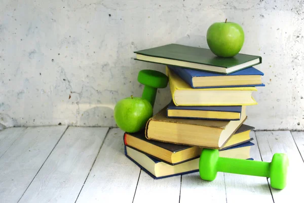 A stack of books, dumbbells and apple on a white background. The concept of combining knowledge, healthy food and sports. The concept of a healthy life and education. Home education concept.