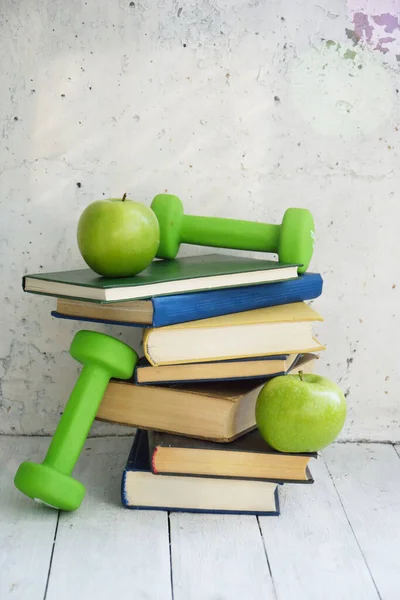 A stack of books, dumbbells and apple on a white background. The concept of combining knowledge, healthy food and sports. The concept of a healthy life and education. Home education concept.