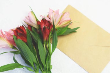 Kırmızı ve pembe alstromerya çiçekleri ve beyaz arka planda el işi posta zarfları. Uzayı kopyala Alstroemeria - Perulu Zambak.