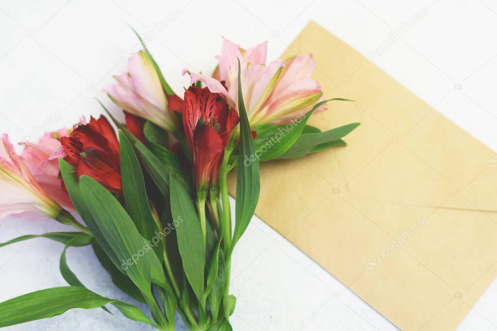 Bouquet of red and pink alstroemeria flowers and craft paper postal envelope on a white background. Copy space. Alstroemeria - Peruvian Lily.
