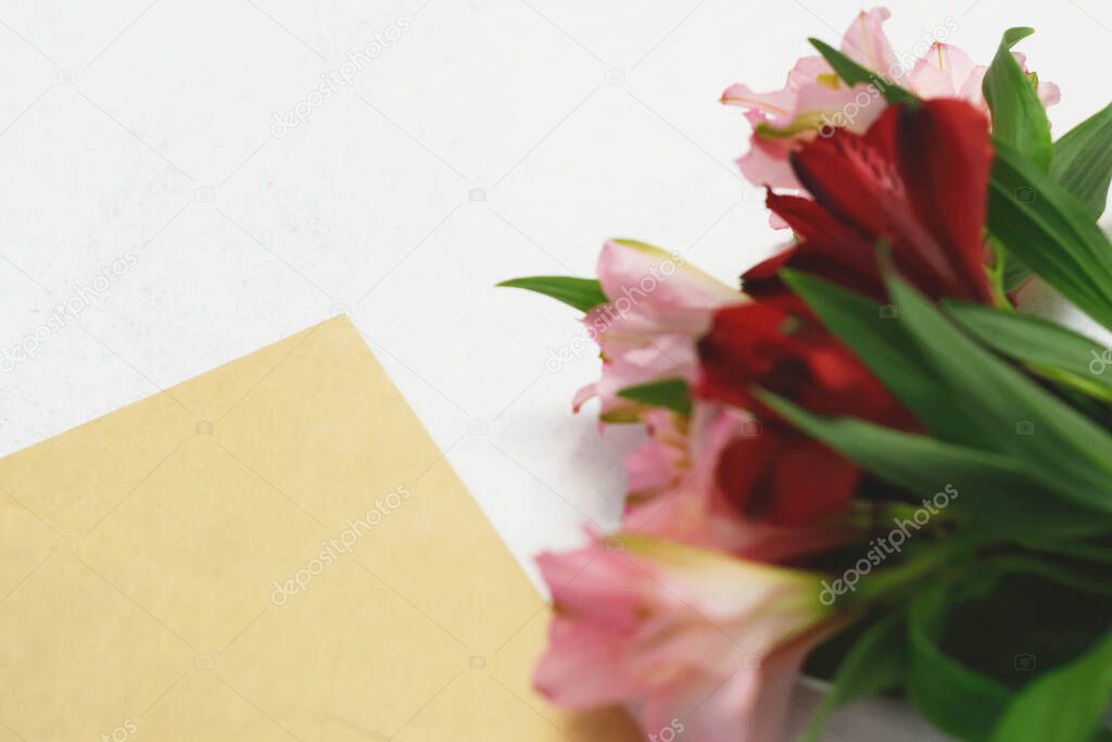 Bouquet of red and pink alstroemeria flowers and craft paper postal envelope on a white background. Copy space. Alstroemeria - Peruvian Lily.